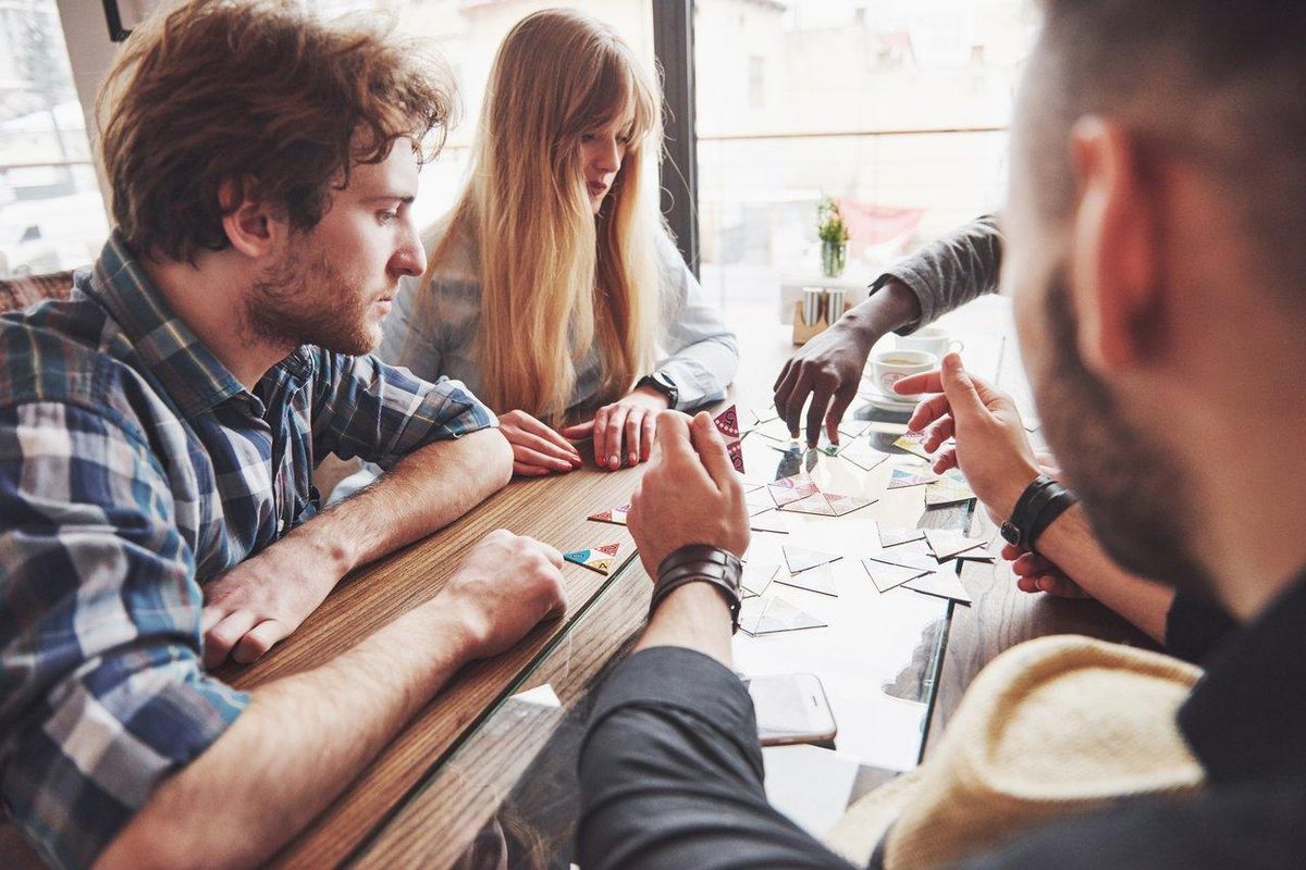 Atelier de création artisanale dans un board game workshop, où des amis diversifiés conçoivent des jeux de société innovants.