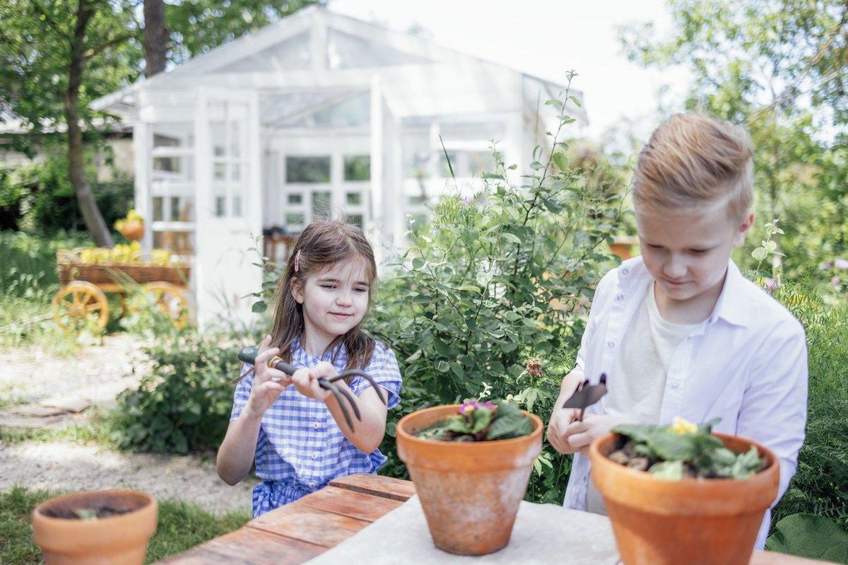 Atelier de jardin extérieur pour enfants : deux jeunes plantant des fleurs dans leur jardin miniature.
