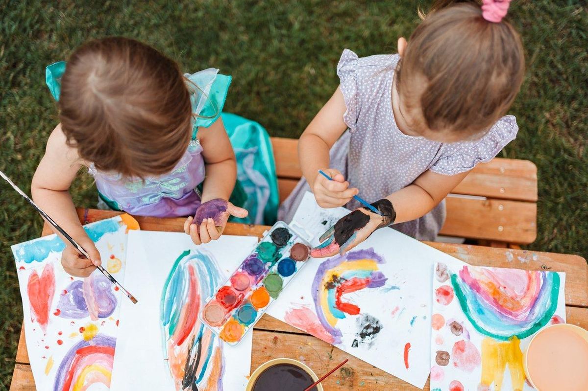 Deux petites filles réalisant des activités créatives en plein air, comme peindre des arcs-en-ciel dans le jardin.