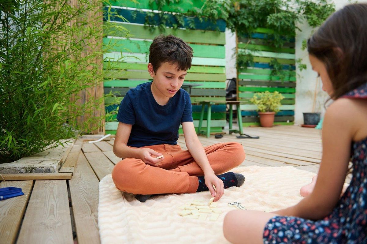 Enfants jouant à un jeu de société adapté à leur âge en plein air sur une terrasse en bois.