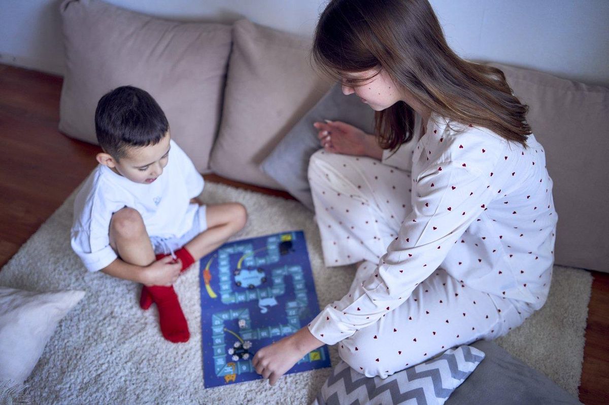 Enfants jouant à un jeu de société sous la supervision bienveillante d’un adulte, favorisant leur développement émotionnel.
