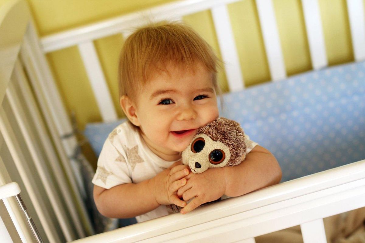 Un bébé souriant câline un doudou en toute sécurité dans une nurserie lumineuse et rassurante.