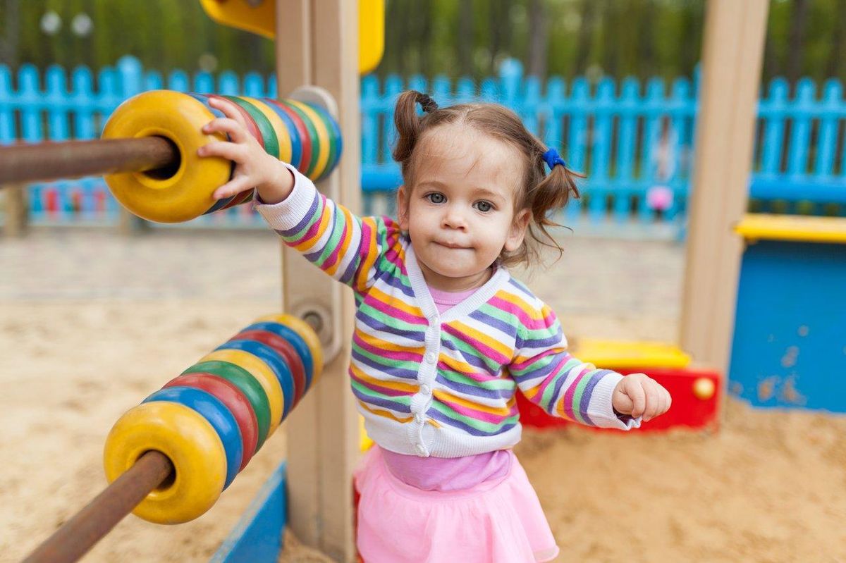 Une enfant jouant dehors avec un jeu sensoriel coloré dans un parc, favorisant le jeu en plein air.