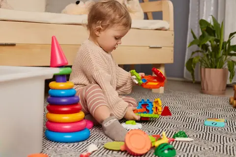 Bébé fille jouant avec des jouets arc-en-ciel colorés, favorisant l’éveil et le développement précoce.