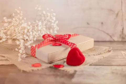 Coffret cadeau Saint-Valentin avec cœur rouge et ruban sur table en bois.
