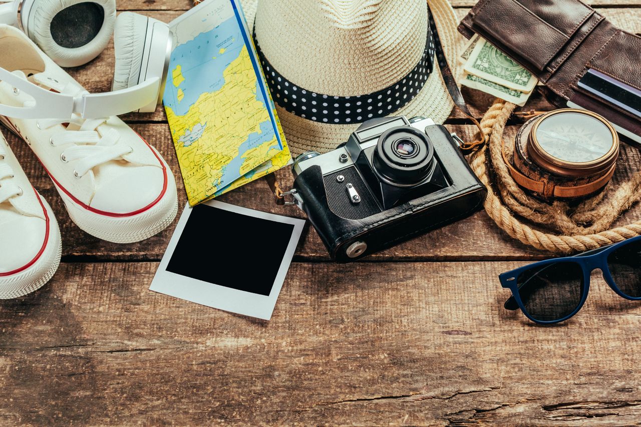 Accessoires de voyage sur une table en bois : carte, boussole, appareil photo et chapeau.