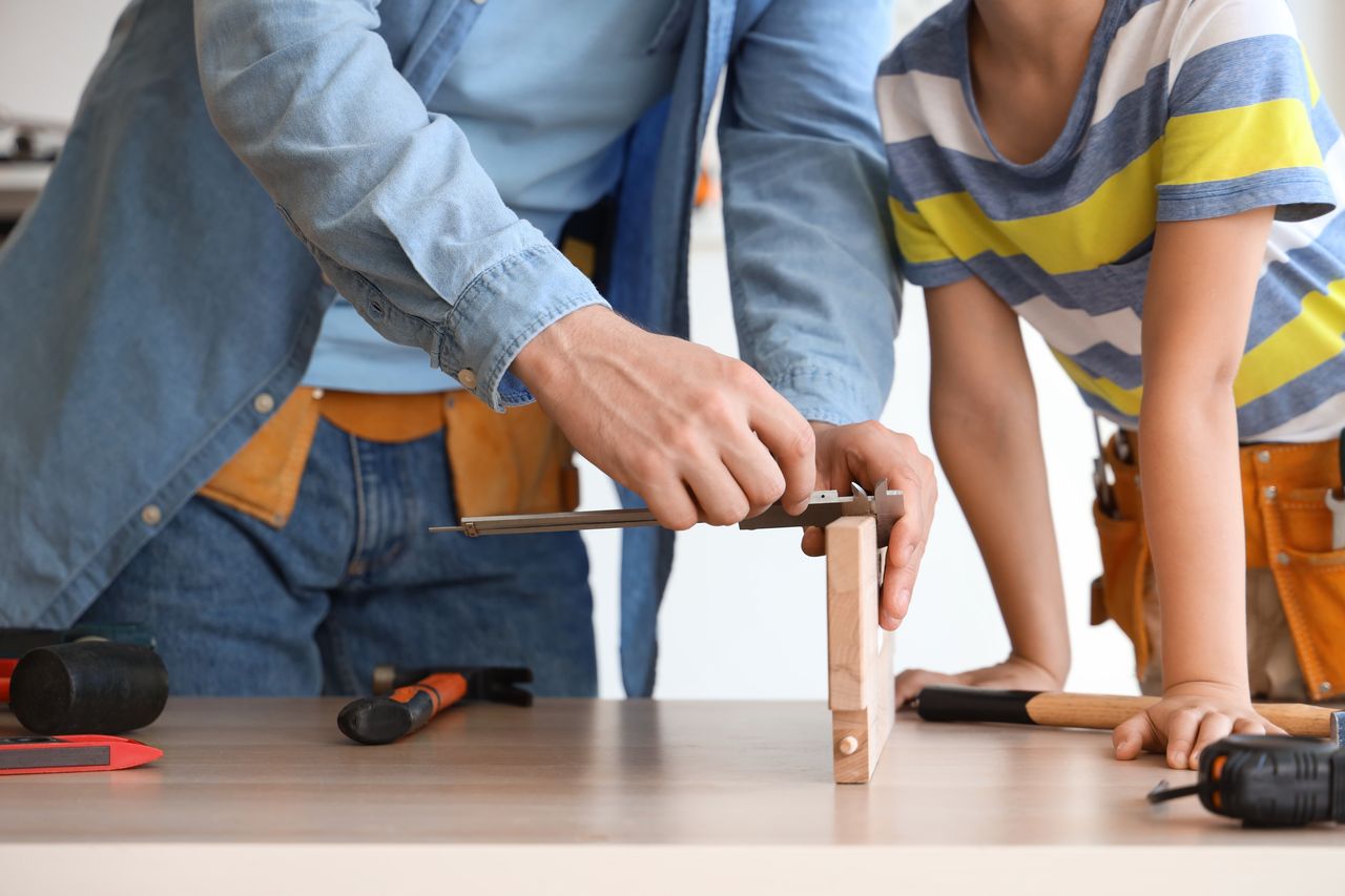 Ado et parent assemblant une maquette en bois sur une table, ambiance chaleureuse et conviviale.