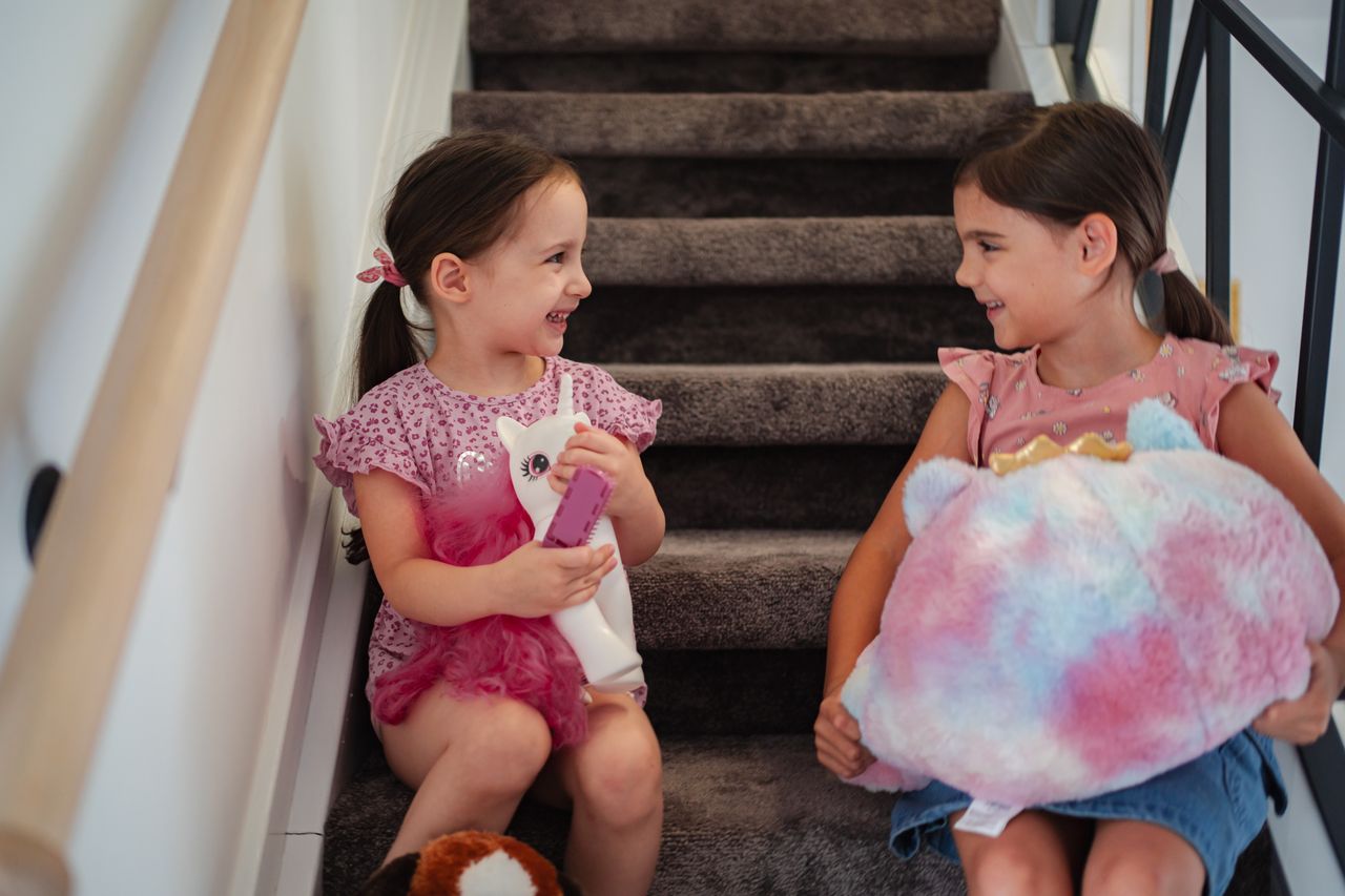 Deux petites filles jouent avec des jouets My Little Pony sur un escalier, en toute complicité.