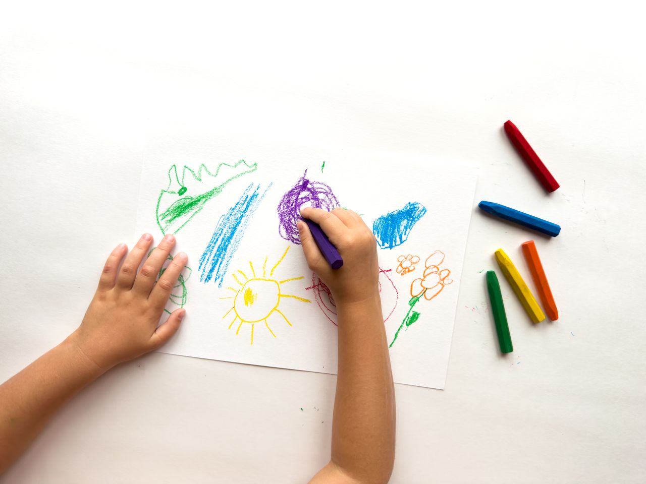 Enfant de 3 à 6 ans dessinant avec des crayons colorés sur du papier blanc.
