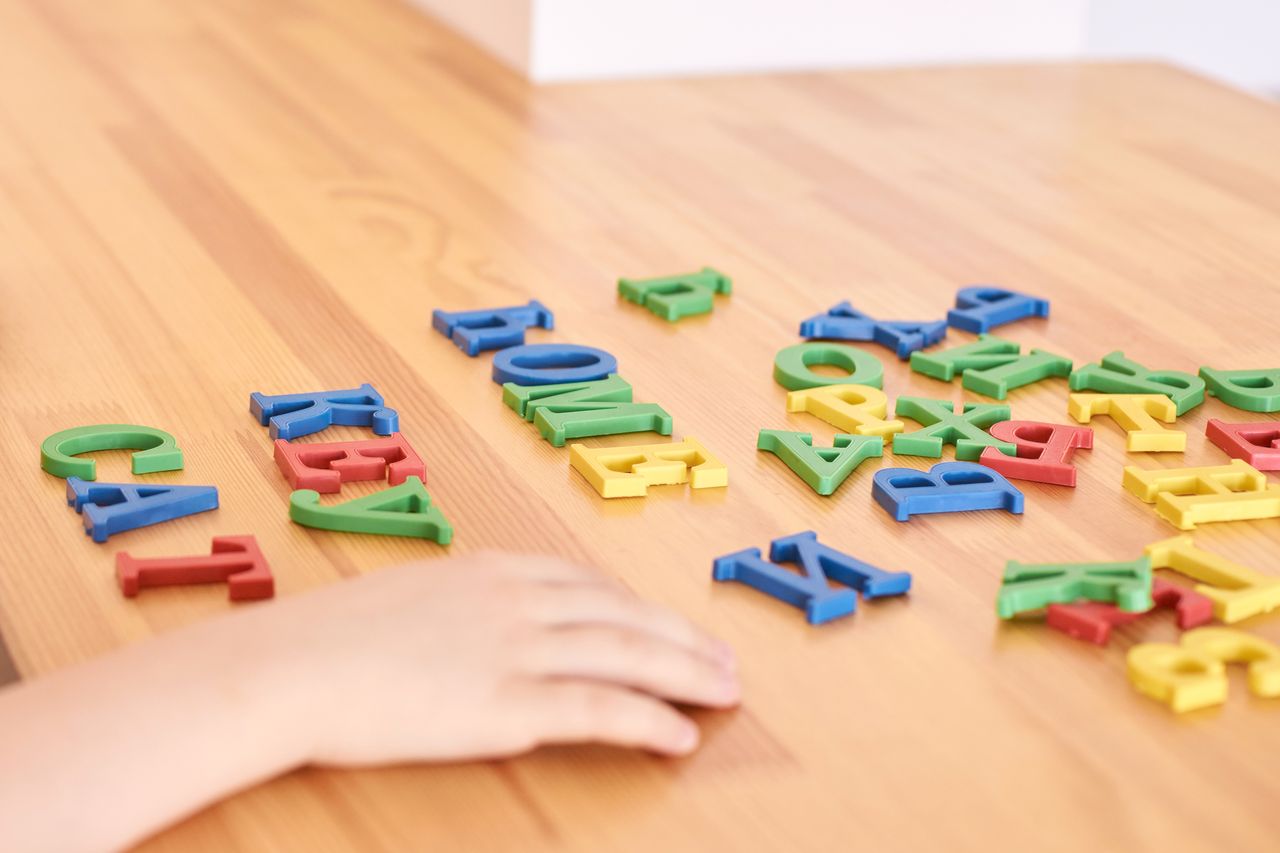 Enfant de 6 ans jouant avec des lettres en papier colorées sur une table familiale en bois.