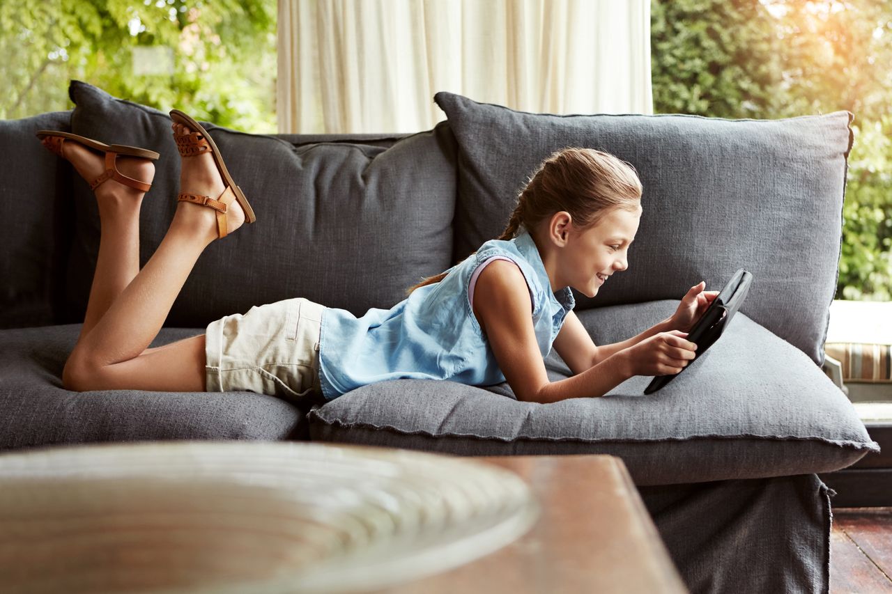 Enfant souriant sur canapé, jouant sur tablette avec Netflix Playground et personnages jeunesse éducatifs.