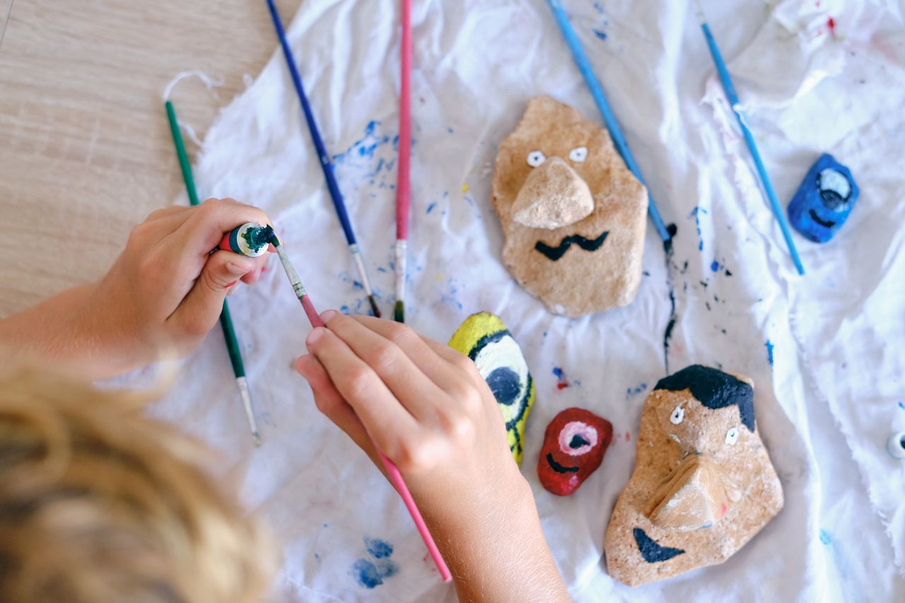 Enfants bricolant des marionnettes en carton, rouleaux recyclés, galets peints et fleurs pressées sur table d’été.