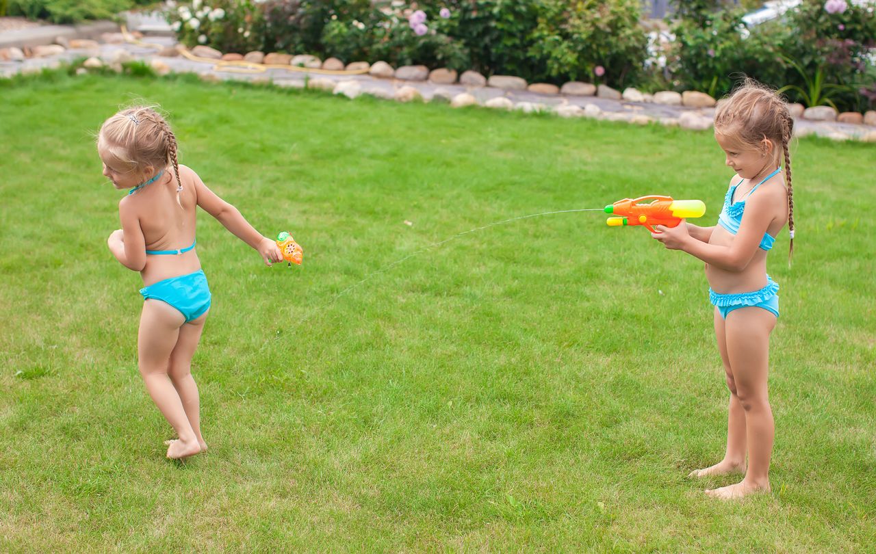 Enfants jouant à des jeux d’eau maison dans le jardin avec éponges, bouteilles, tuyaux et bassine.