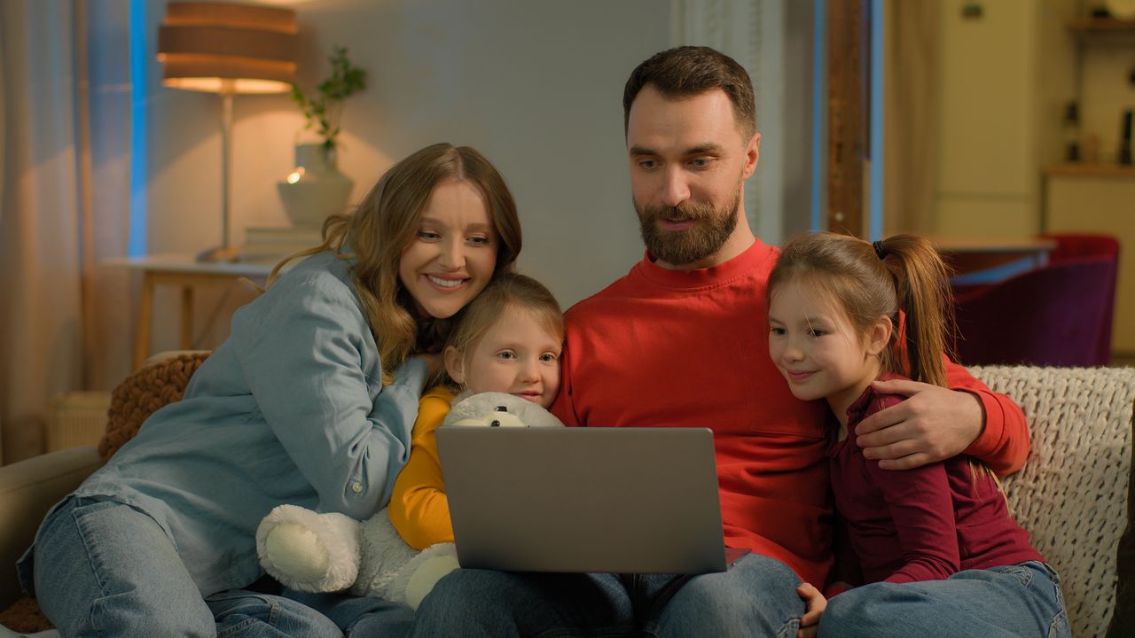 Famille caucasienne jouant à un jeu vidéo coopératif sur PC dans un salon chaleureux le soir