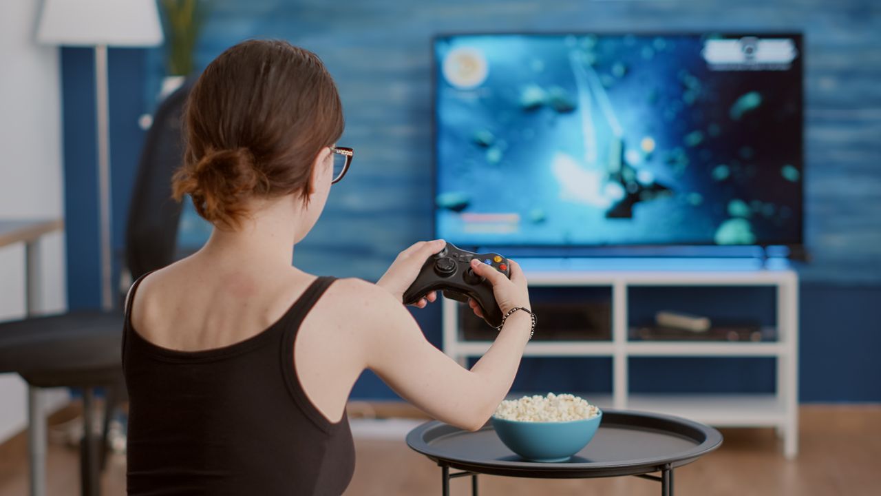 Femme joueuse célébrant une victoire sur console avec manette devant un grand écran TV.