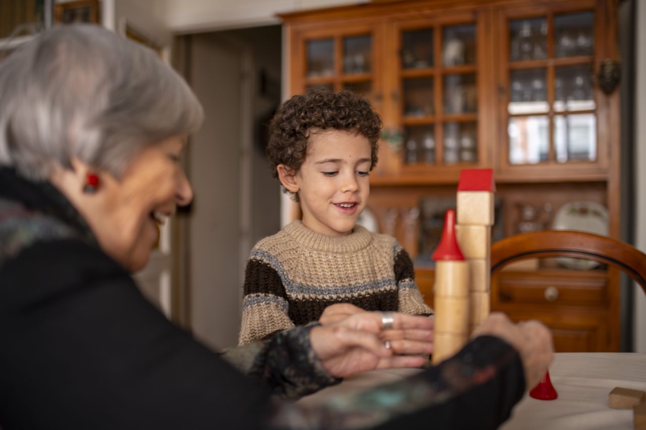 Grand-mère et enfant construisent un château en bois, un jeu créatif idéal pour les 6-8 ans.