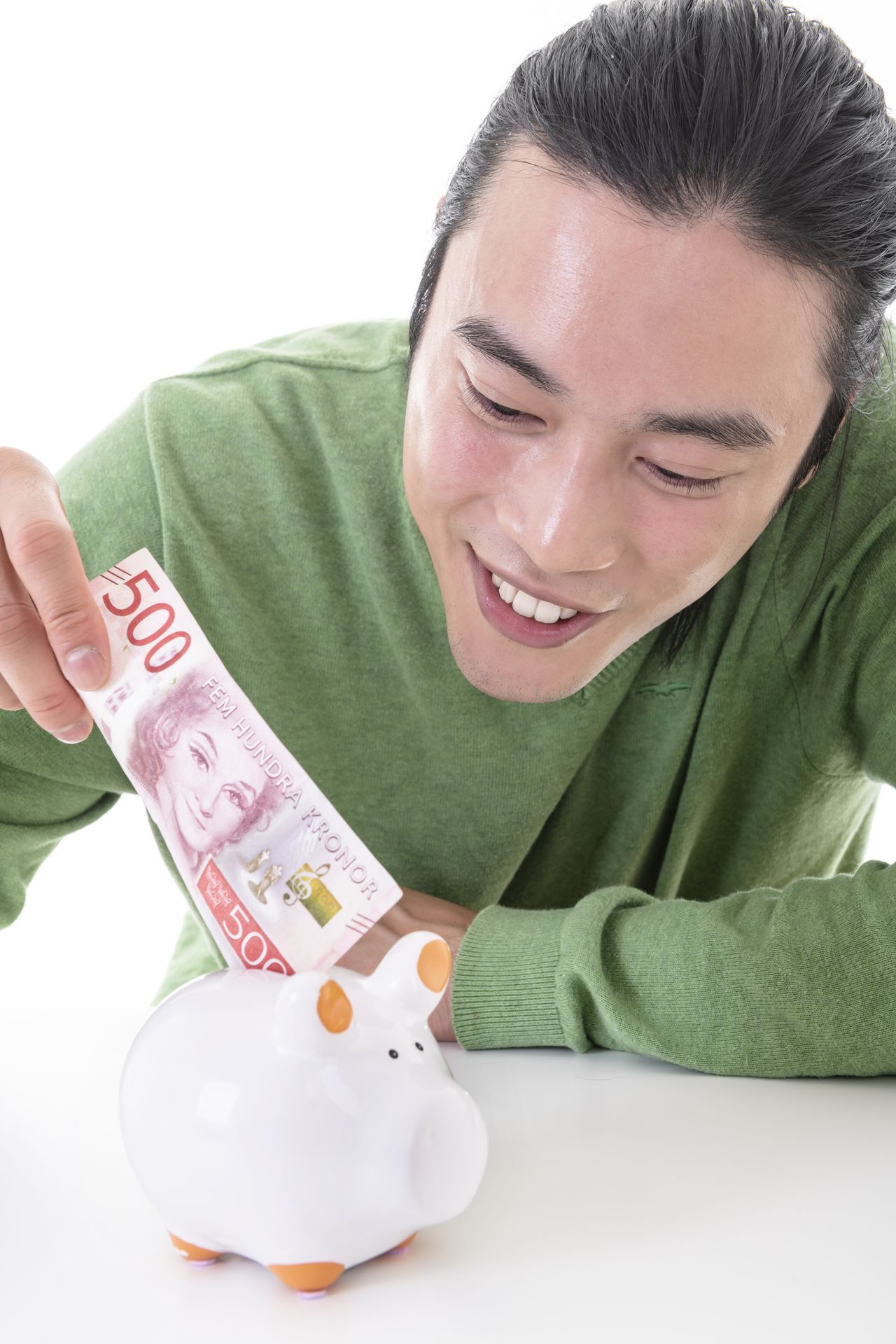 Homme asiatique souriant déposant de l’argent dans une tirelire à la maison