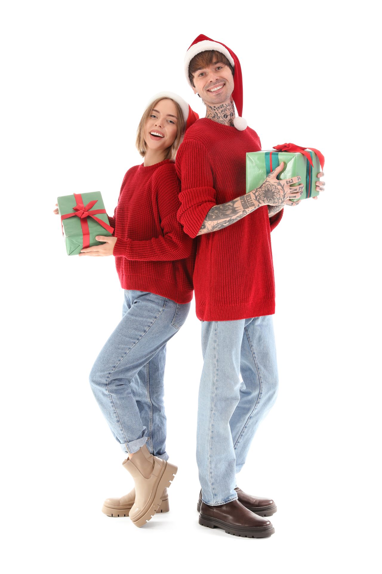 Jeune couple heureux en tenue de Noël, entouré de boîtes cadeaux sur fond blanc.