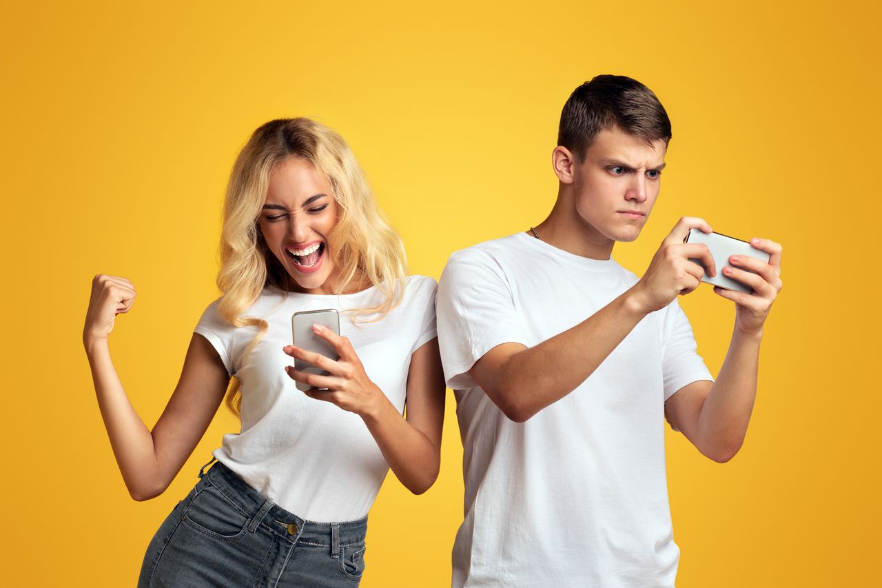 Jeune couple jouant à des jeux mobiles sur smartphone, célébrant une victoire ensemble.