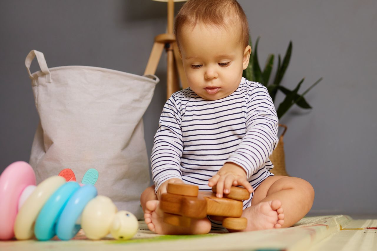 Jeune enfant jouant sur un tapis doux, entouré de jouets colorés et de blocs en bois éducatifs.