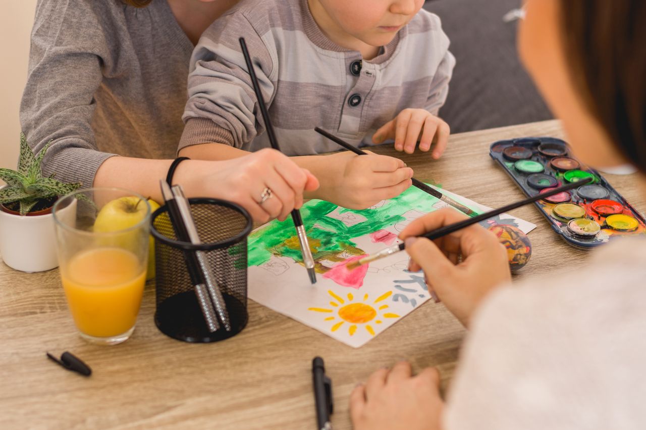 Maman et enfants peignent ensemble avec des aquarelles pour une activité créative en famille.