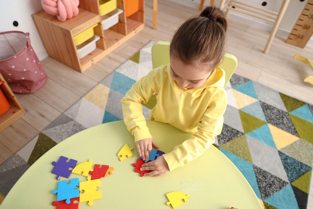 Petite fille assemblant un puzzle coloré à la maison, vue de dessus sur une table.