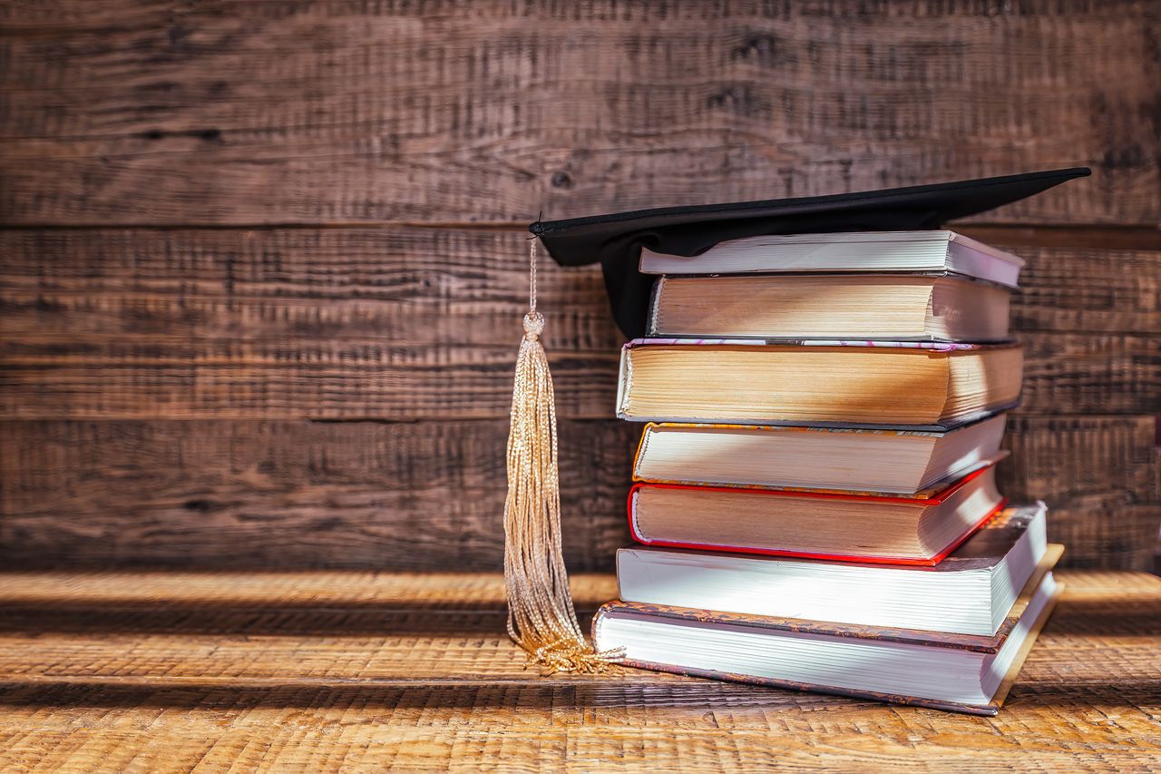 Toque de diplômé posée sur des livres, symbole de réussite scolaire et d’études sur fond en bois