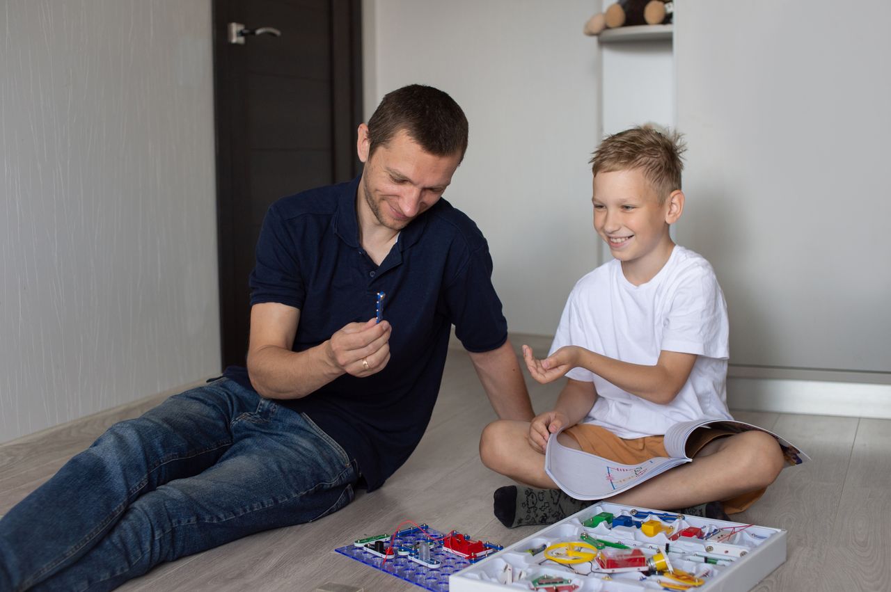 Un garçon heureux assemble un jeu de construction électrique avec son père à la maison