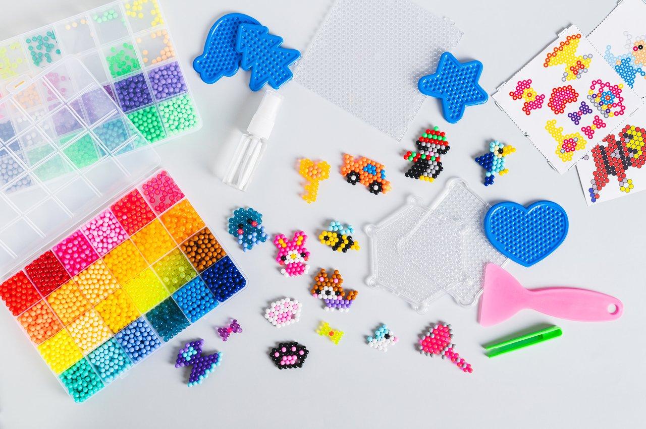 Enfant créant un motif avec des perles à repasser colorées, idéale pour développer la motricité fine chez les 4-8 ans.