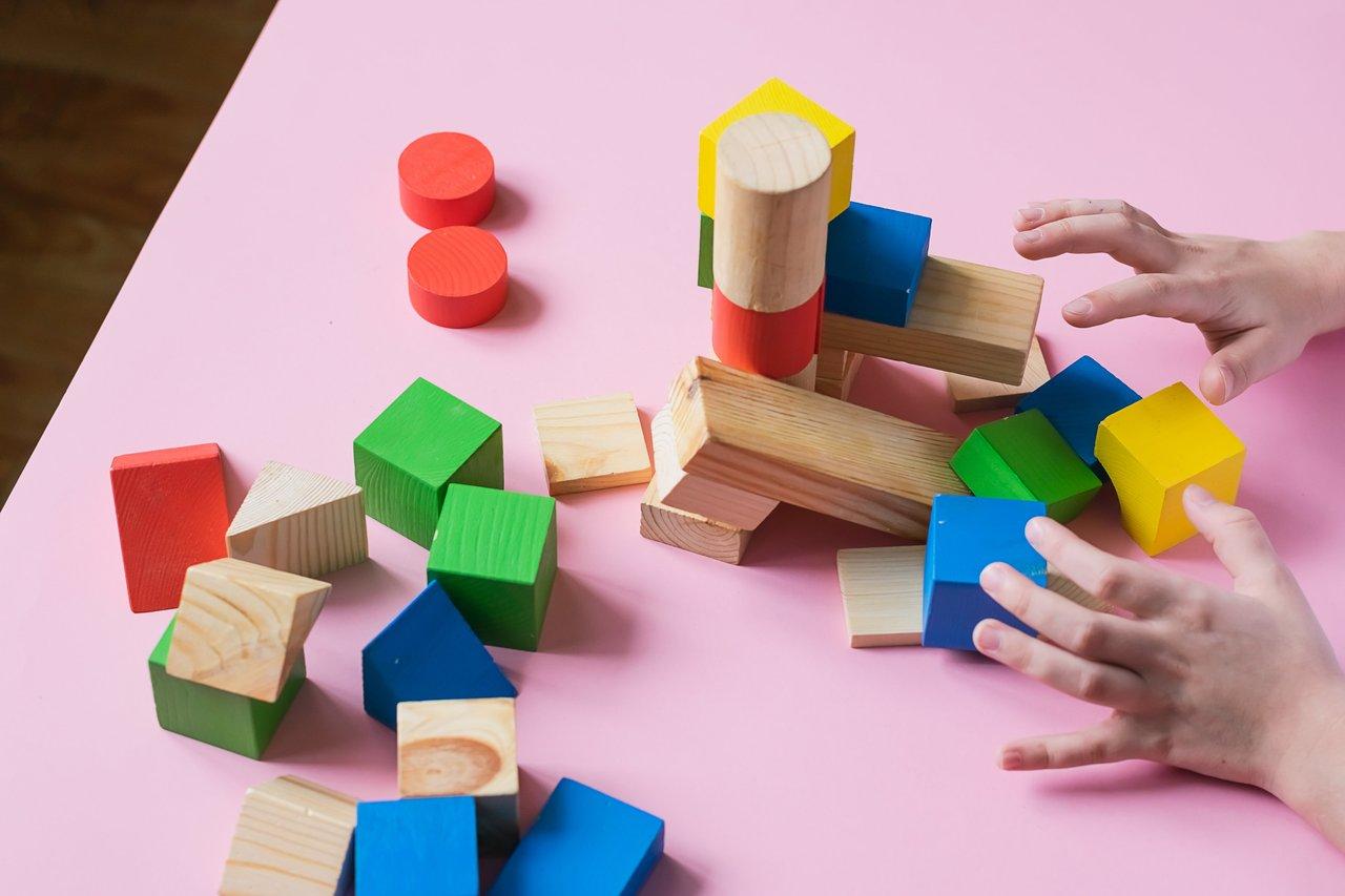 Enfants construisant une maison en blocs de bois lors d’un atelier avec un animateur, une activité ludique et éducative.