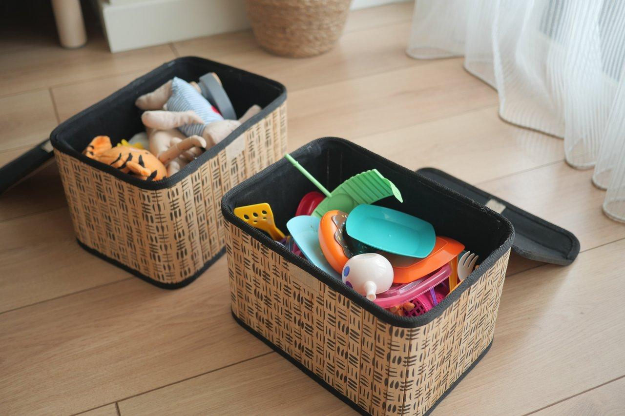 Un coffre en bois bien organisé dans une chambre d’enfant avec des jouets rangés dans des paniers colorés à côté d'une fenêtre.