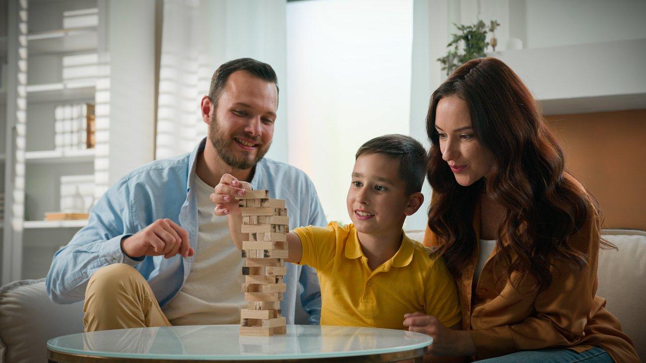 Une famille heureuse joue ensemble à un jeu de société en bois coloré, idéale pour les enfants de 6 à 10 ans.