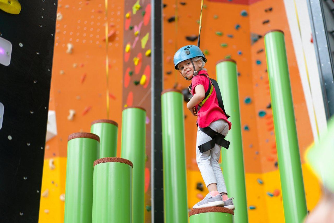 Une jeune fille en équipement de sécurité pratique l'escalade en intérieur, assurant une child indoor climbing safety optimale.